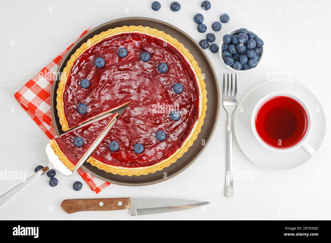 Cheesecake maison avec gelée de baies et une tasse d'hibiscus de thé rouge sur une table en bois blanc. Vue de dessus. Banque D'Images
