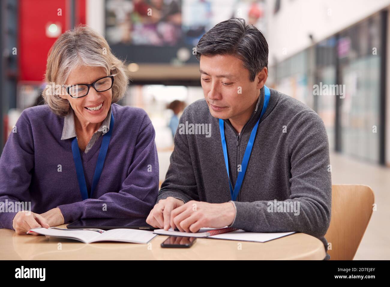 Enseignant avec un étudiant adulte de sexe masculin mature assis à la table de travail Dans College Hall Banque D'Images