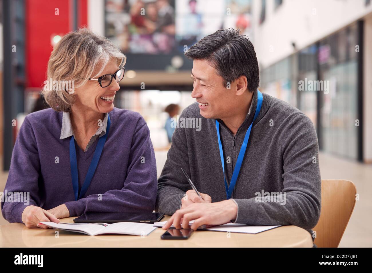 Enseignant avec un étudiant adulte de sexe masculin mature assis à la table de travail Dans College Hall Banque D'Images
