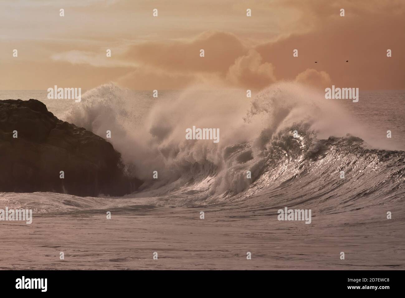 Une vague qui se brise au coucher du soleil. Côte rocheuse portugaise du nord du pays. Ciel amélioré. Banque D'Images