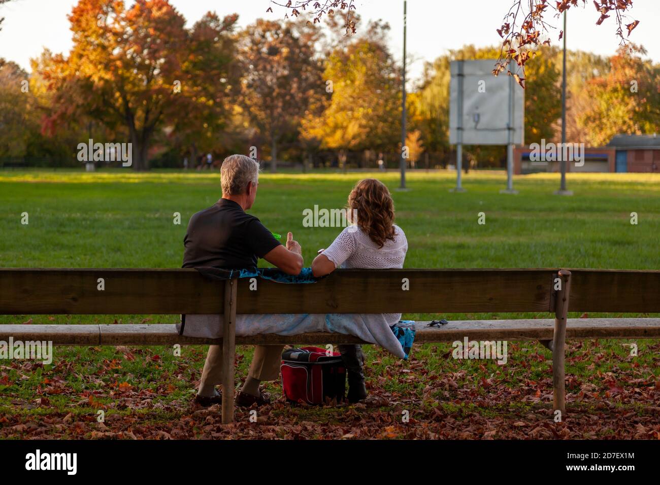 Un couple caucasien d'âge moyen est assis sur un banc en bois dans un parc couvert de feuilles mortes au coucher du soleil. Un concept d'automne pittoresque avec romance et t Banque D'Images