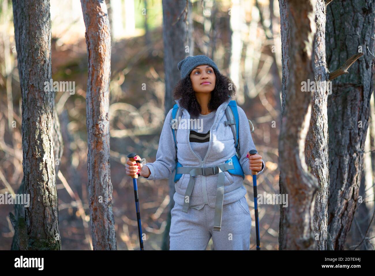 Photo d'une femme afro-américaine marchant dans la forêt.femme avec des bâtons de marche nordique et un sac à dos. Banque D'Images