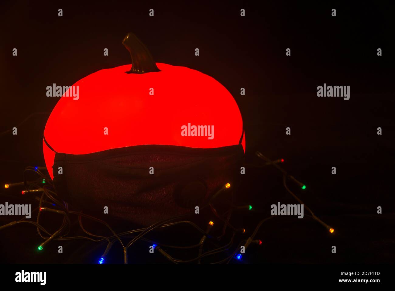 Citrouille d'Halloween en terre cuite brillante effrayante sans yeux portant un masque sur fond noir avec des lumières. Fête d'Halloween 2020 avec COVID-19 Banque D'Images