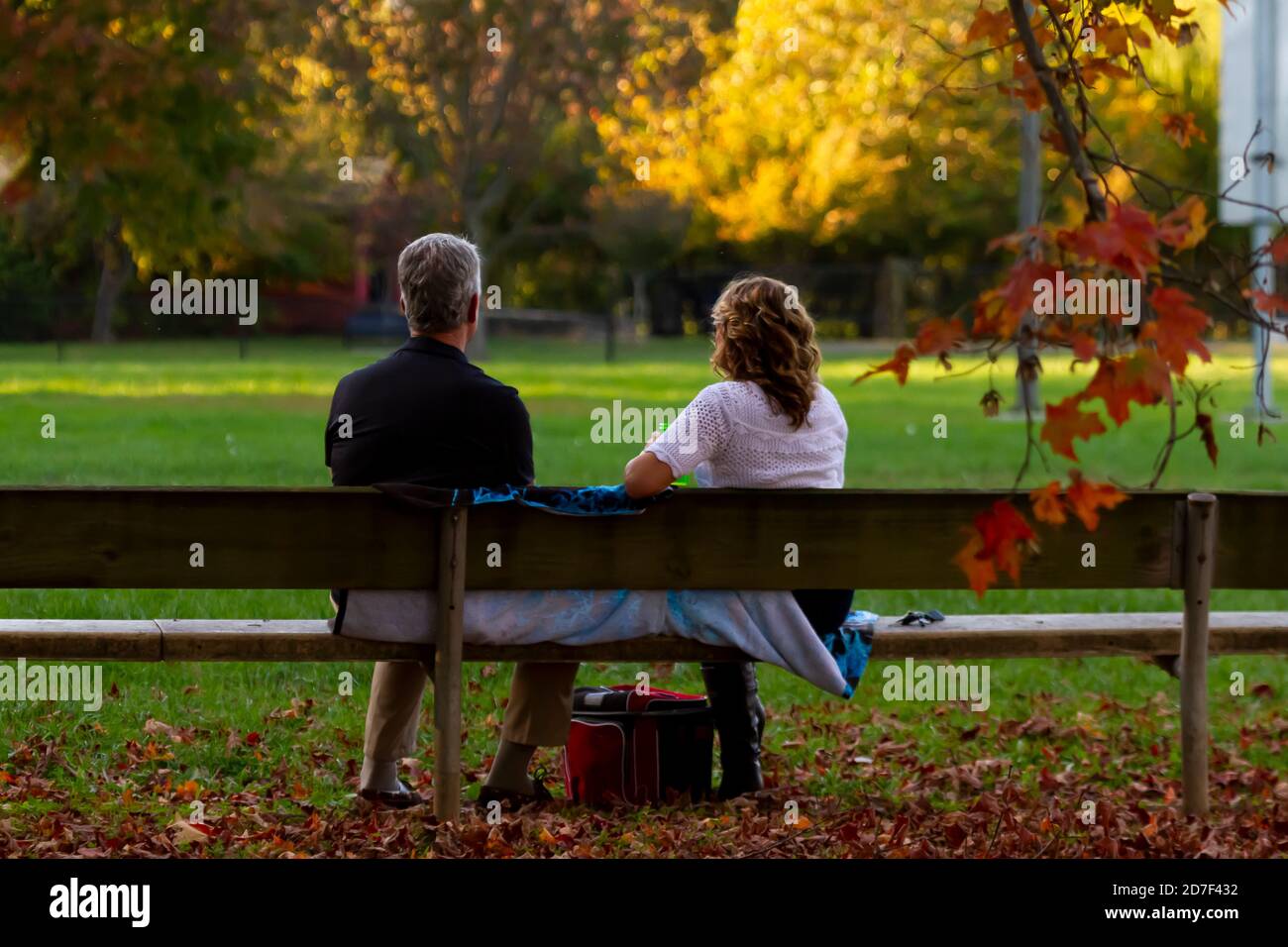 Un couple caucasien d'âge moyen est assis sur un banc en bois dans un parc couvert de feuilles mortes au coucher du soleil. Un concept d'automne pittoresque avec romance et t Banque D'Images