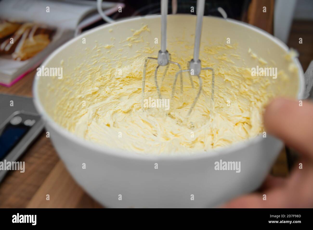 Un homme tient un mixeur plongeant électrique. Il mélange le beurre, les oeufs et le sucre. Une petite pâtisserie est préparée. Gros plan depuis la cuisine. Banque D'Images