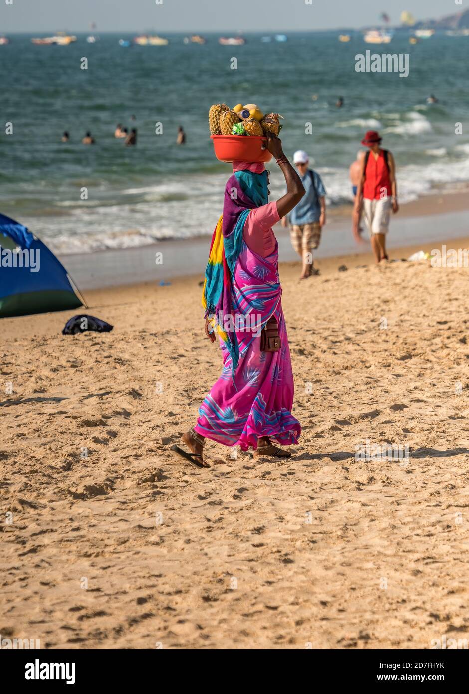 Femme indienne non identifiée en rose coloré bleu sari robe portant des fruits frais dans le bassin rouge à sa tête pour vendre à la rive aux touristes. Ensoleillé Banque D'Images