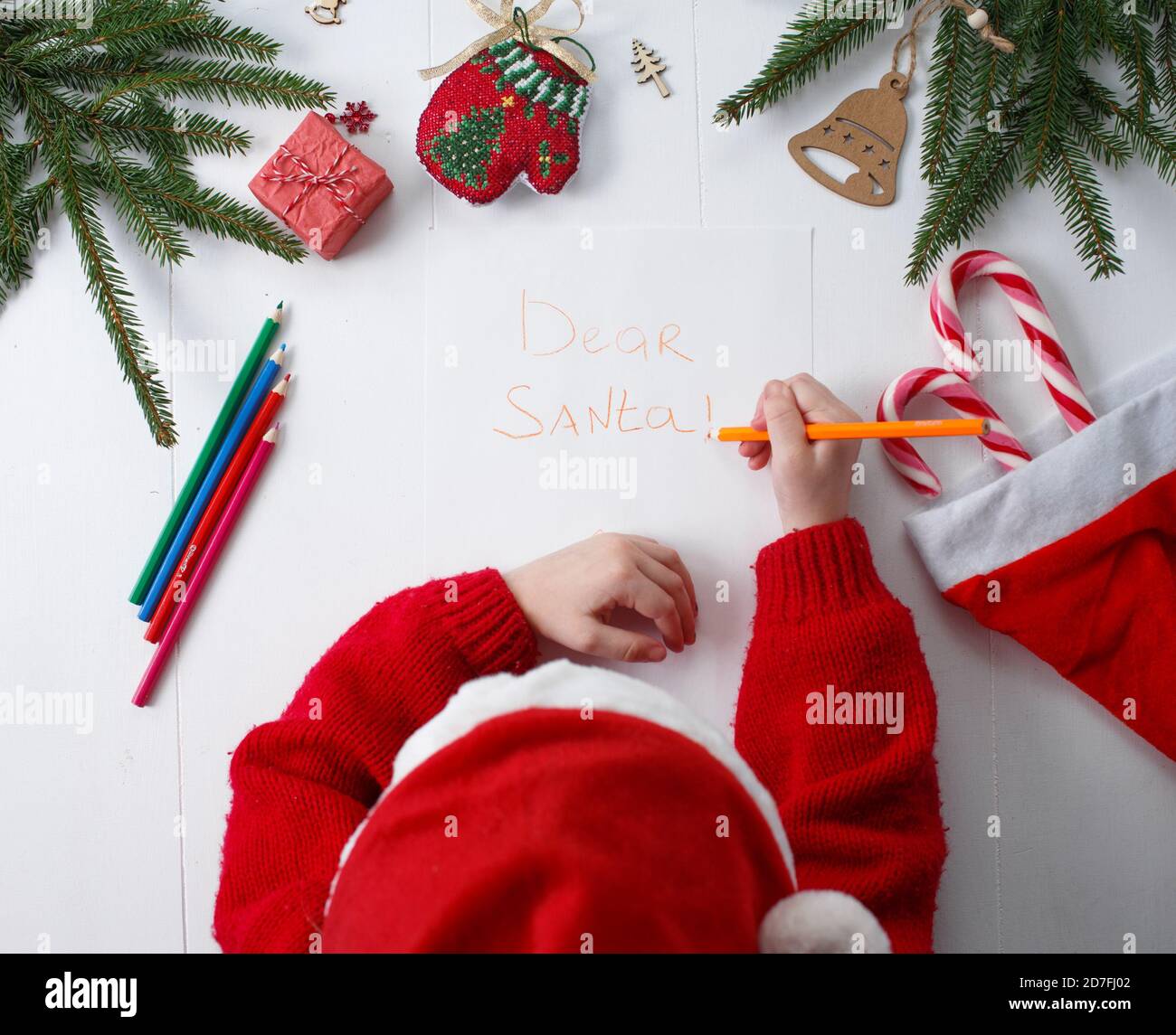 L'enfant écrit la lettre au Père Noël. Les mains des enfants, la feuille de papier, les crayons et les décorations de Noël sur une surface en bois. Concept de la nouvelle année Banque D'Images