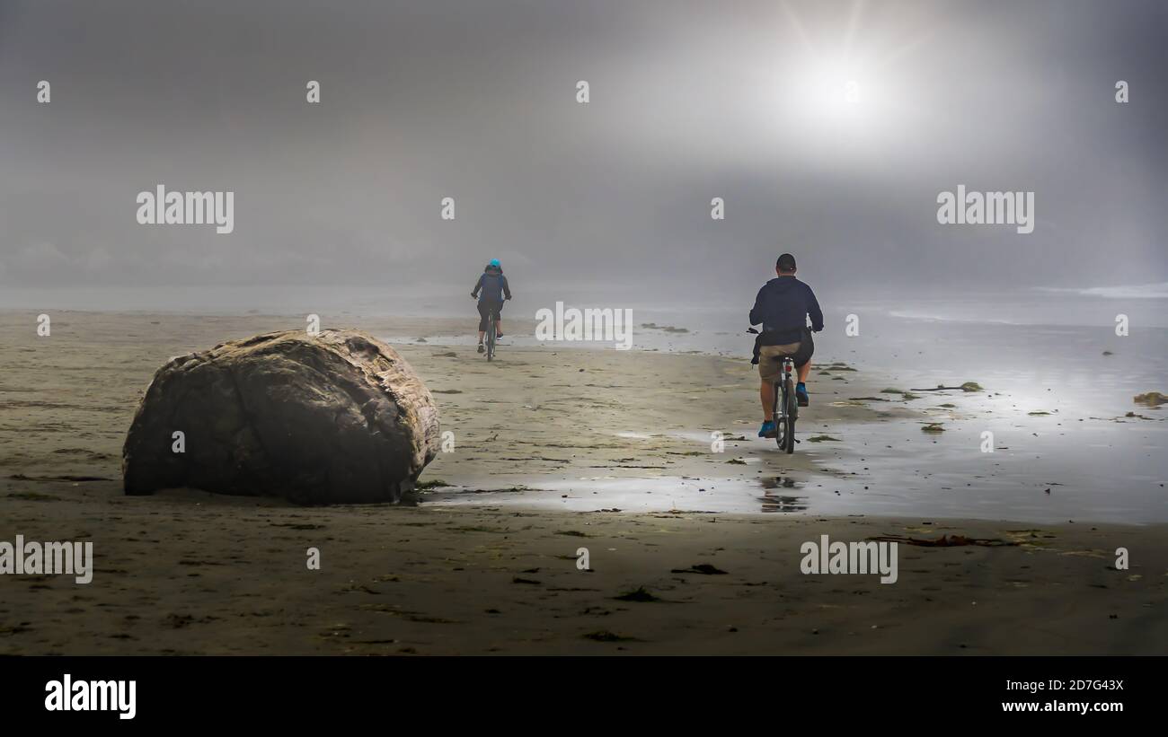 Les cyclistes qui font du brouillard dense font du vélo sur la plage de Cox Bay, au parc national Pacific Rim, sur l'île de Vancouver, en Colombie-Britannique, au Canada Banque D'Images