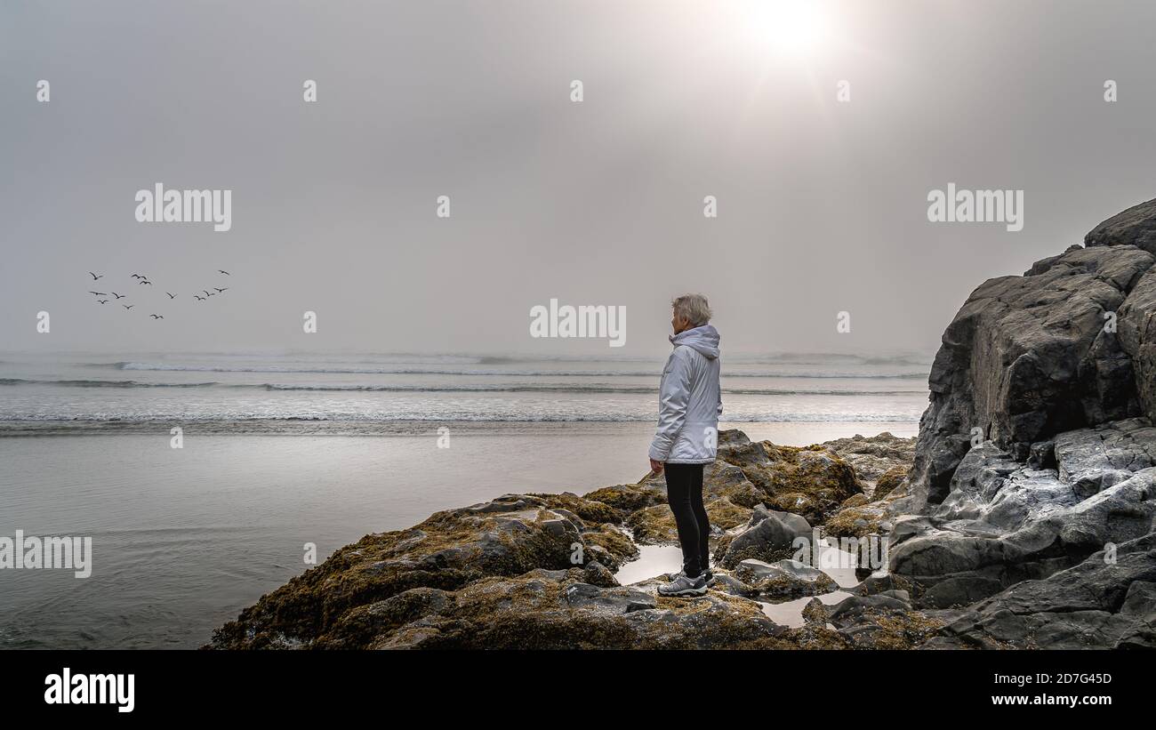 Femme âgée qui regarde dans le brouillard dense au-dessus de l'océan Pacifique à Cox Bay, dans le parc national Pacific Rim, sur l'île de Vancouver, en Colombie-Britannique, Banque D'Images