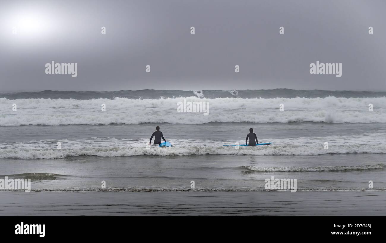 Surfeurs se dirigeant dans les vagues dans le brouillard dense pour surfer dans la baie Cox au parc national Pacific Rim sur l'île de Vancouver, Colombie-Britannique, Canada Banque D'Images
