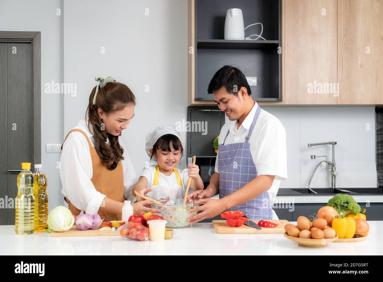 Les jeunes familles d'amour asiatiques préparent des légumes de salade sur la table dans la cuisine à laquelle le père et la mère enseignant la fille cuisiner la journée à Banque D'Images