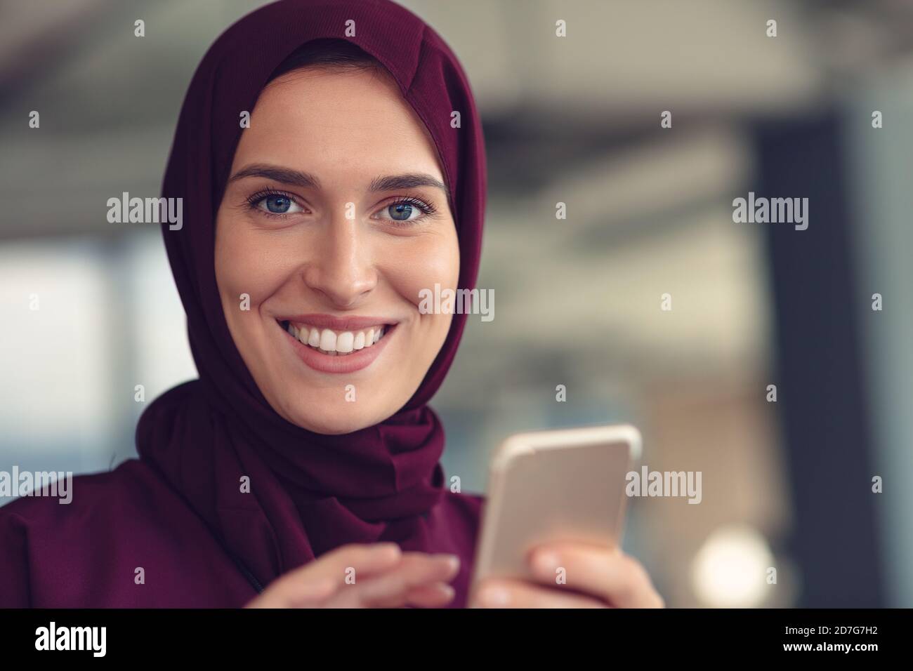 Bonne femme d'affaires musulmane dans le hijab sur le lieu de travail de bureau. Femme arabe souriante travaillant sur un ordinateur portable et utilisant un téléphone portable. Banque D'Images