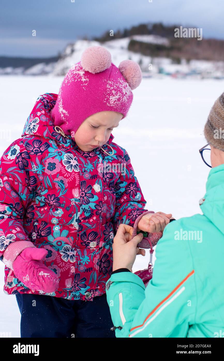 Une fille dans une veste verte met une mitaine sur la main d'une petite  fille tout en marchant dans le parc en hiver. Prendre soin des mains en  hiver. Protection de Photo