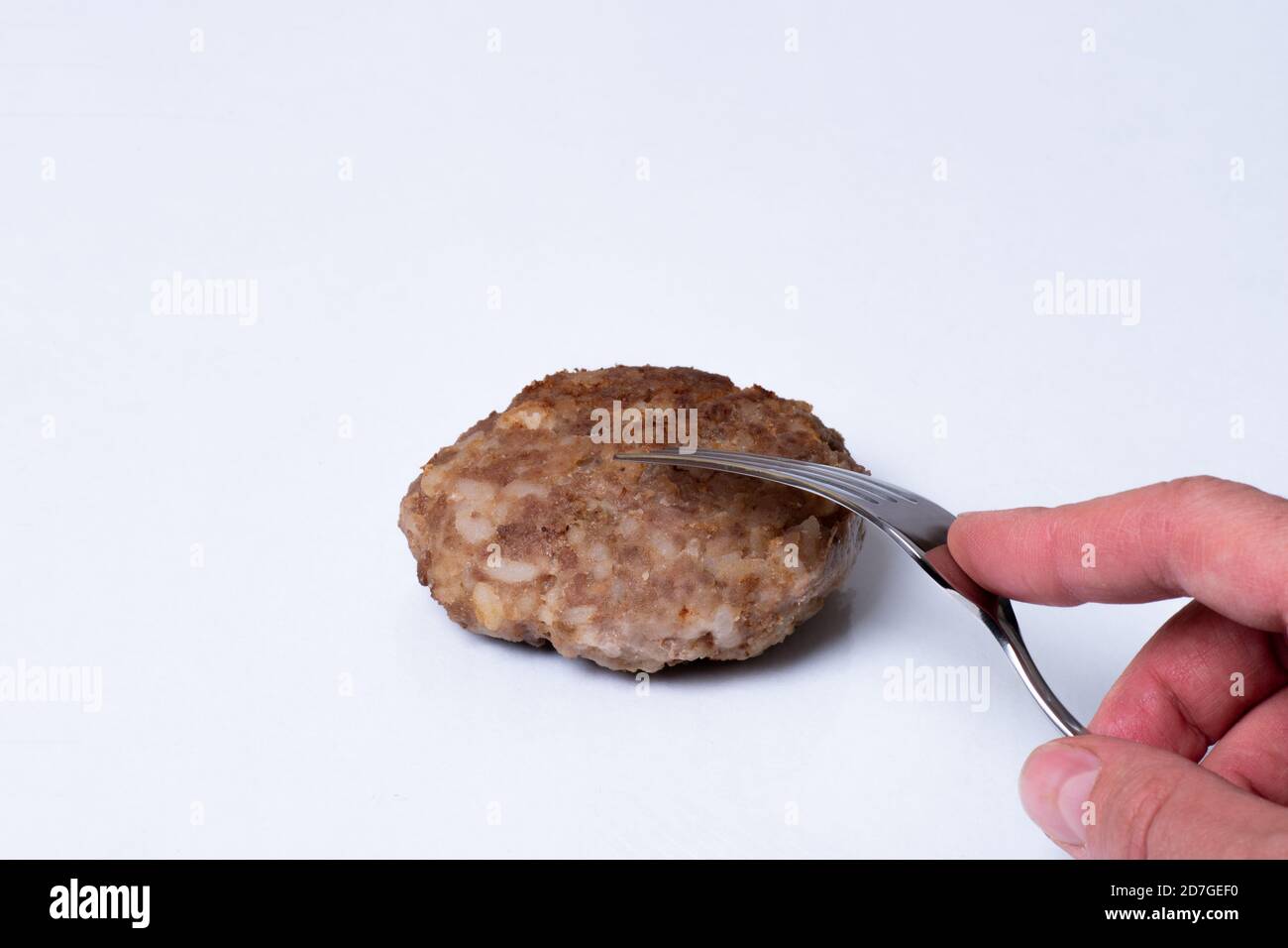 La main tient une fourchette sur une patty de viande cuite sur une plaque blanche isolée sur fond blanc, gros plan, espace de copie Banque D'Images