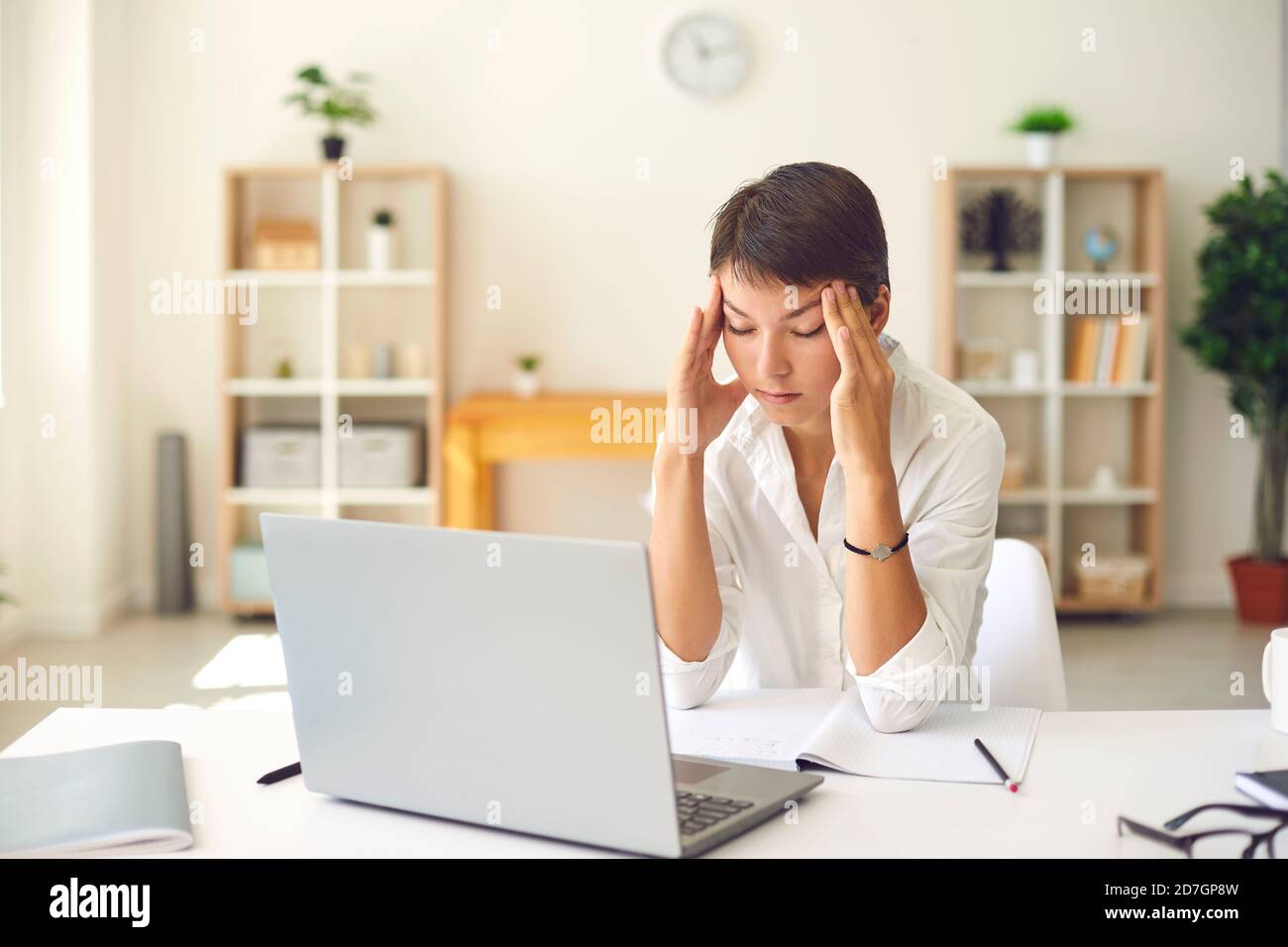 Femme fatiguée avec mal de tête ou vision floue massant les temples salon avec bureau et ordinateur portable Banque D'Images