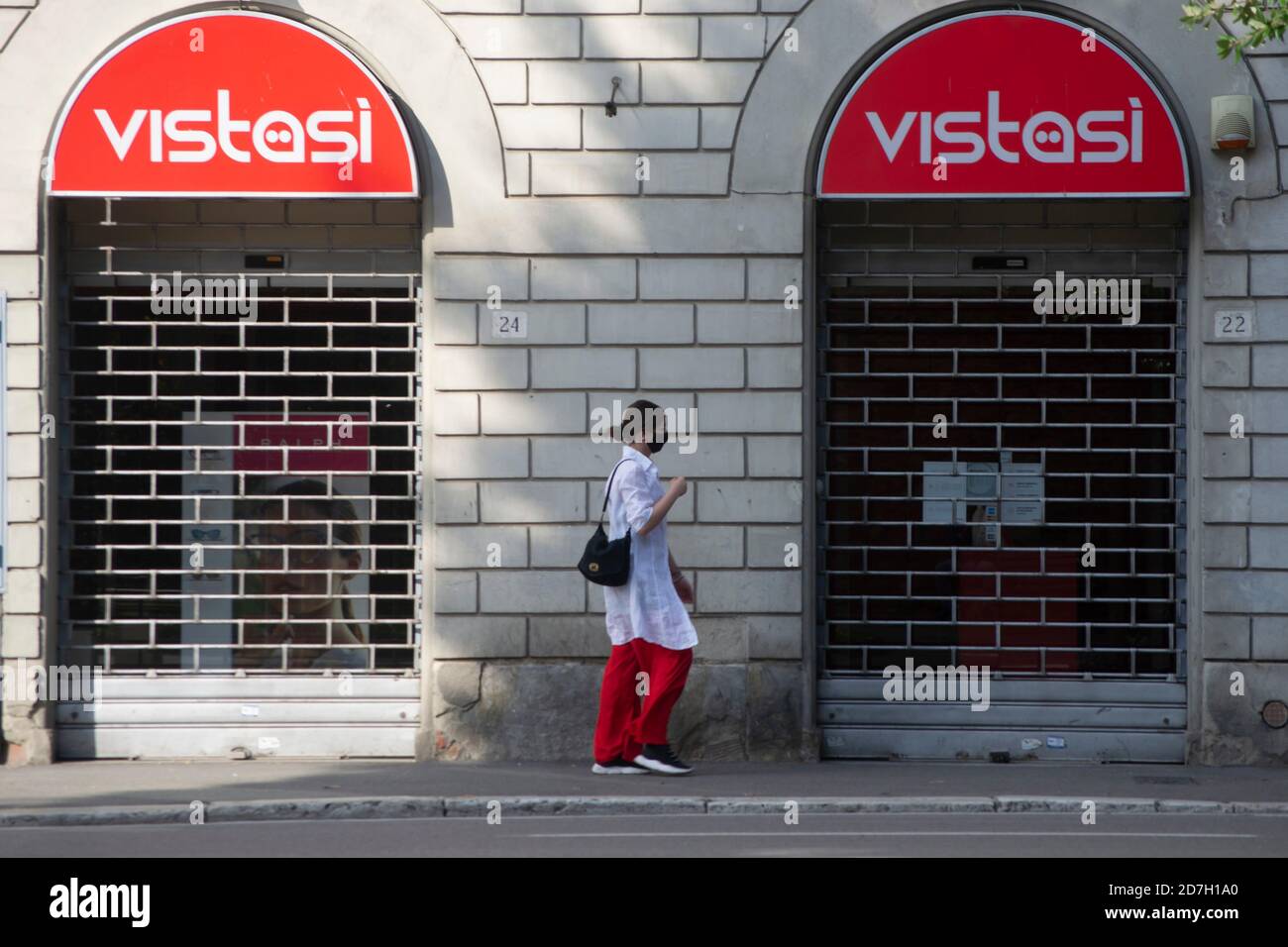 une fille en pantalon rouge et masque marche sur le trottoir d'une rue de ville à côté d'un magasin avec rouge signes Banque D'Images