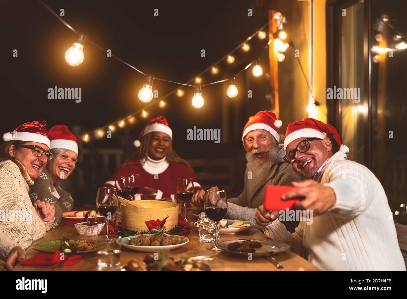 Des amis aînés heureux dînant et célébrant les vacances de Noël tout en prenant selfie avec smartphone mobile sur le patio de la maison fête Banque D'Images