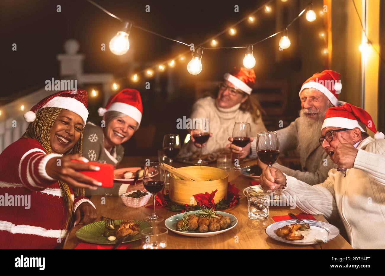 Des amis aînés heureux dînant et célébrant les vacances de Noël en prenant le selfie avec un smartphone mobile sur le patio de la maison Banque D'Images