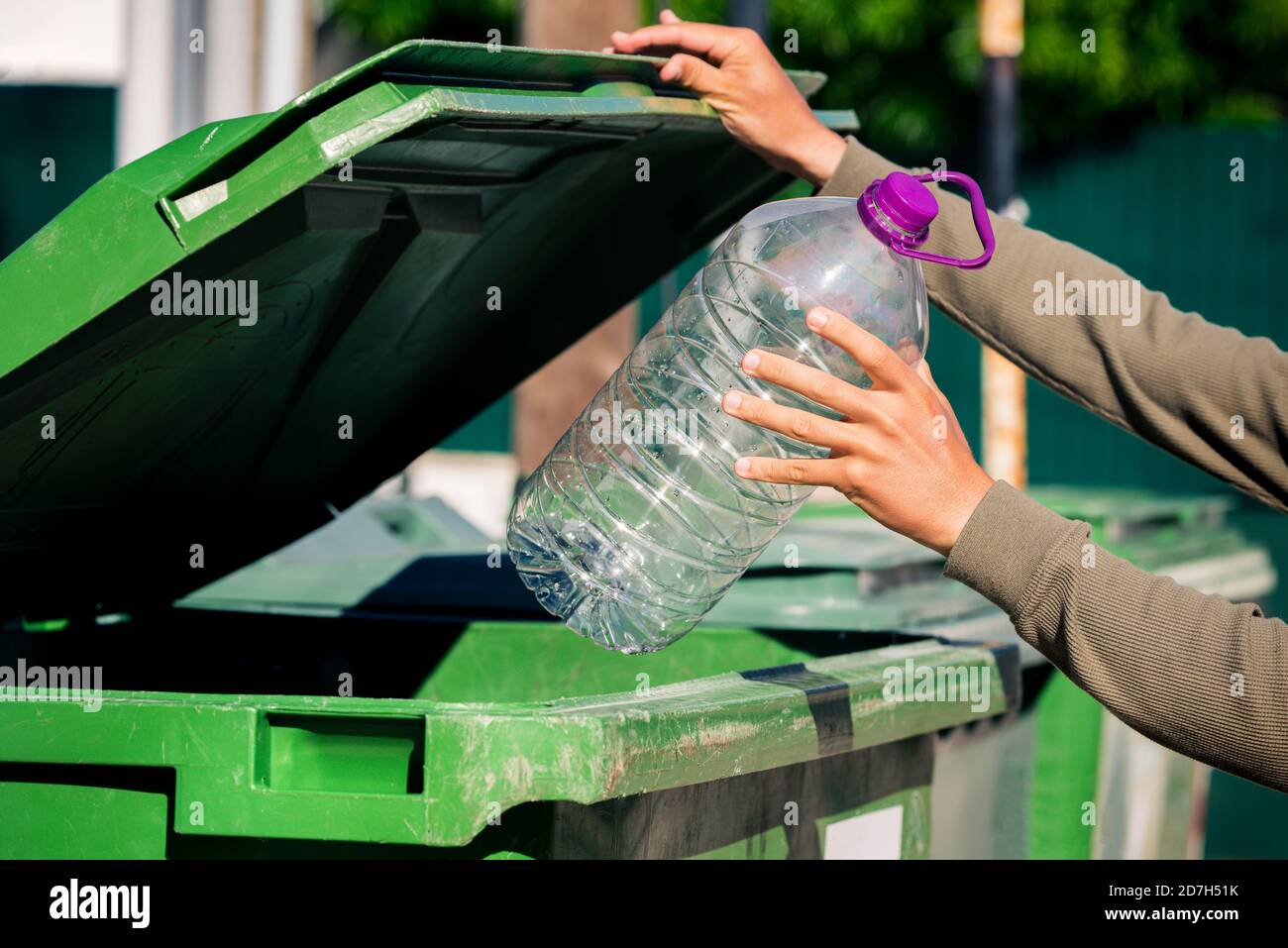 Homme jetant une grande bouteille d'aqua en plastique dans un conteneur à ordures vert. Utilisé une grande bouteille en plastique vide. Banque D'Images