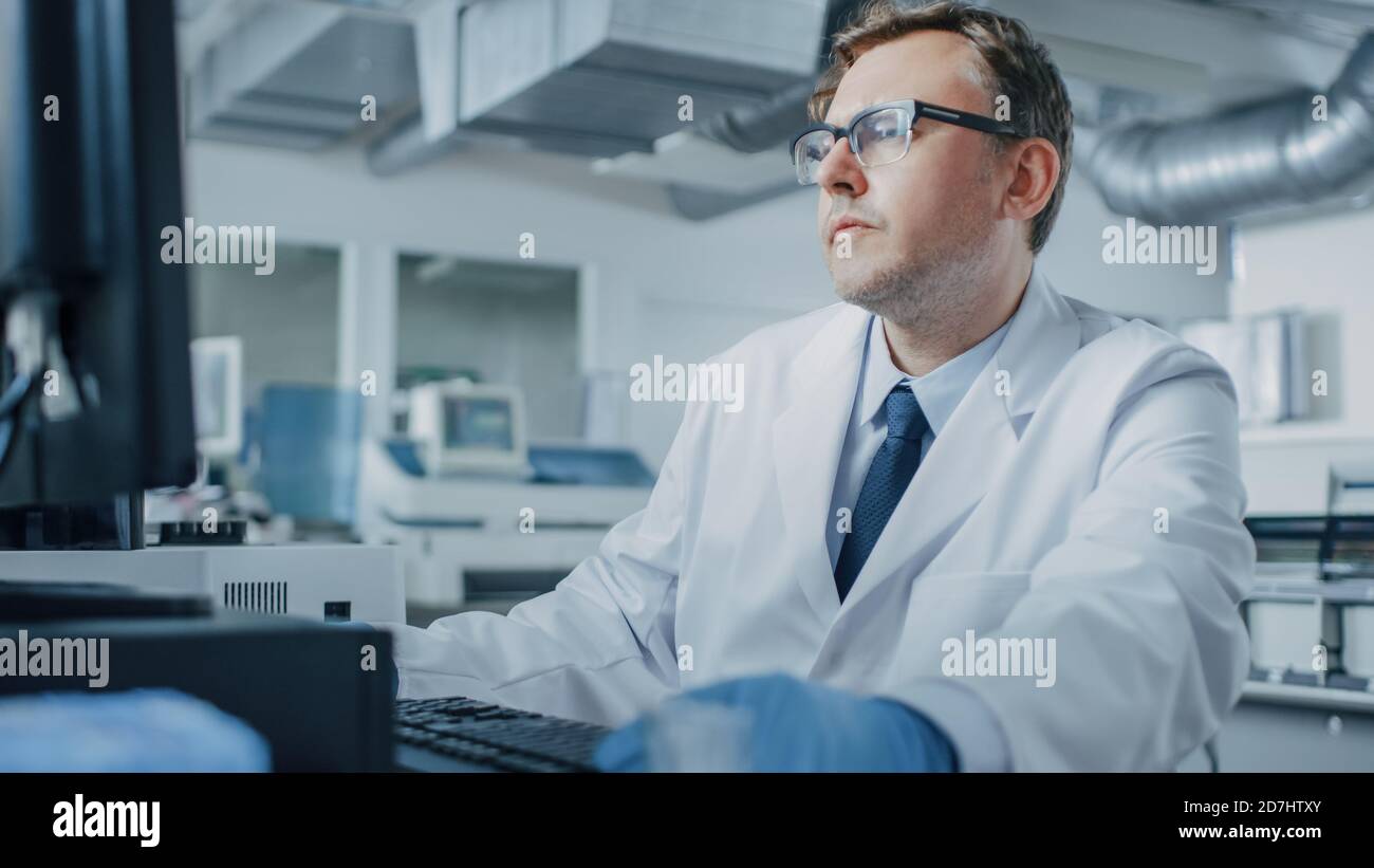 Un scientifique de recherche de sexe masculin est assis dans son milieu de travail en laboratoire et utilise un ordinateur personnel. I la génétique de base, Centre de recherche pharmaceutique avec Banque D'Images