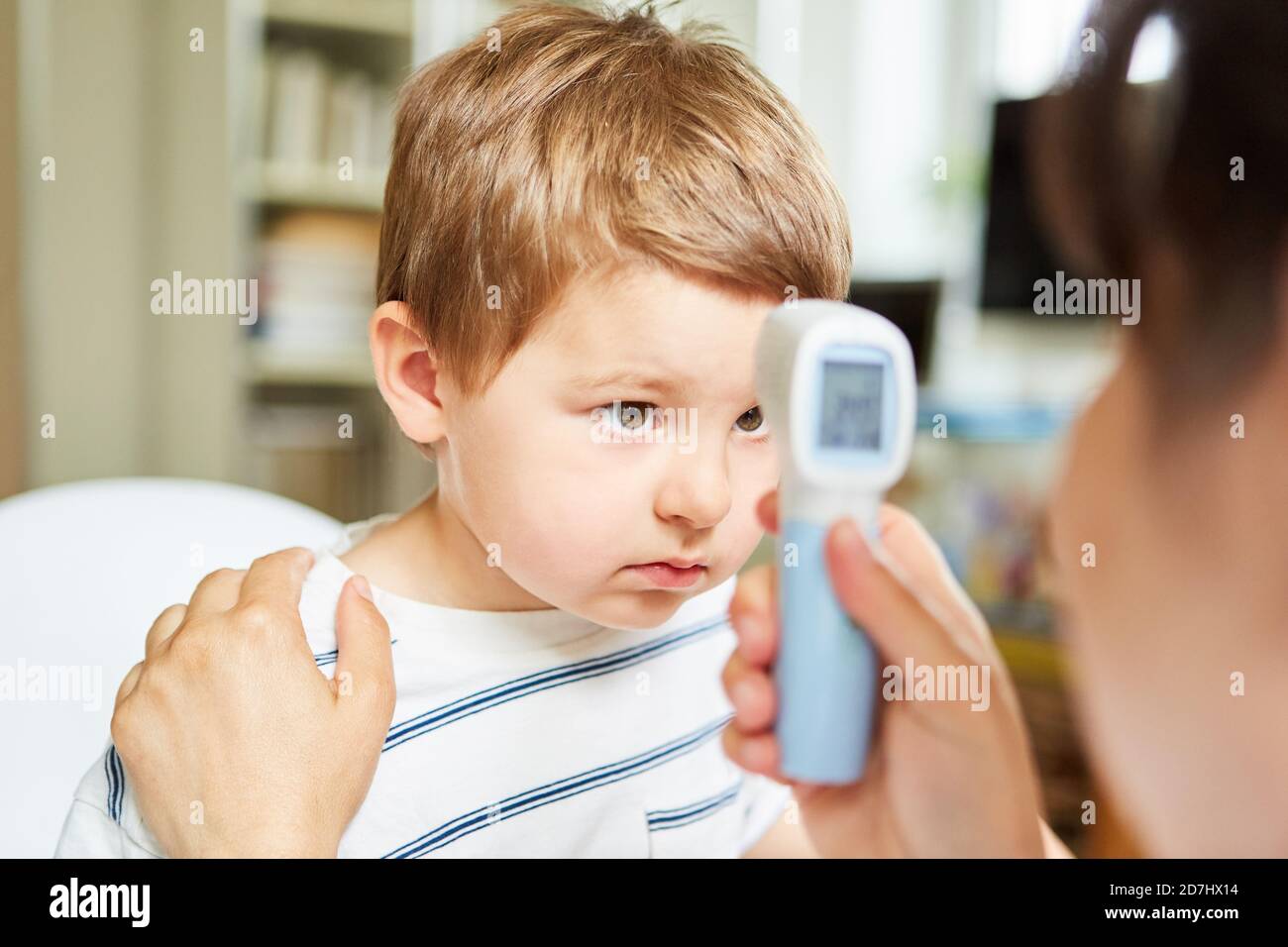 Pédiatre mesurant une fièvre chez un enfant ayant un rhume avec le thermomètre frontal Banque D'Images