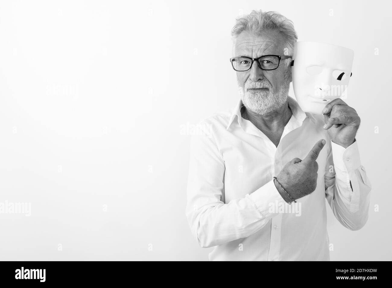 Portrait of senior man holding barbu beau masque blanc près de face et montre de l'index tout en portant des lunettes contre fond blanc Banque D'Images