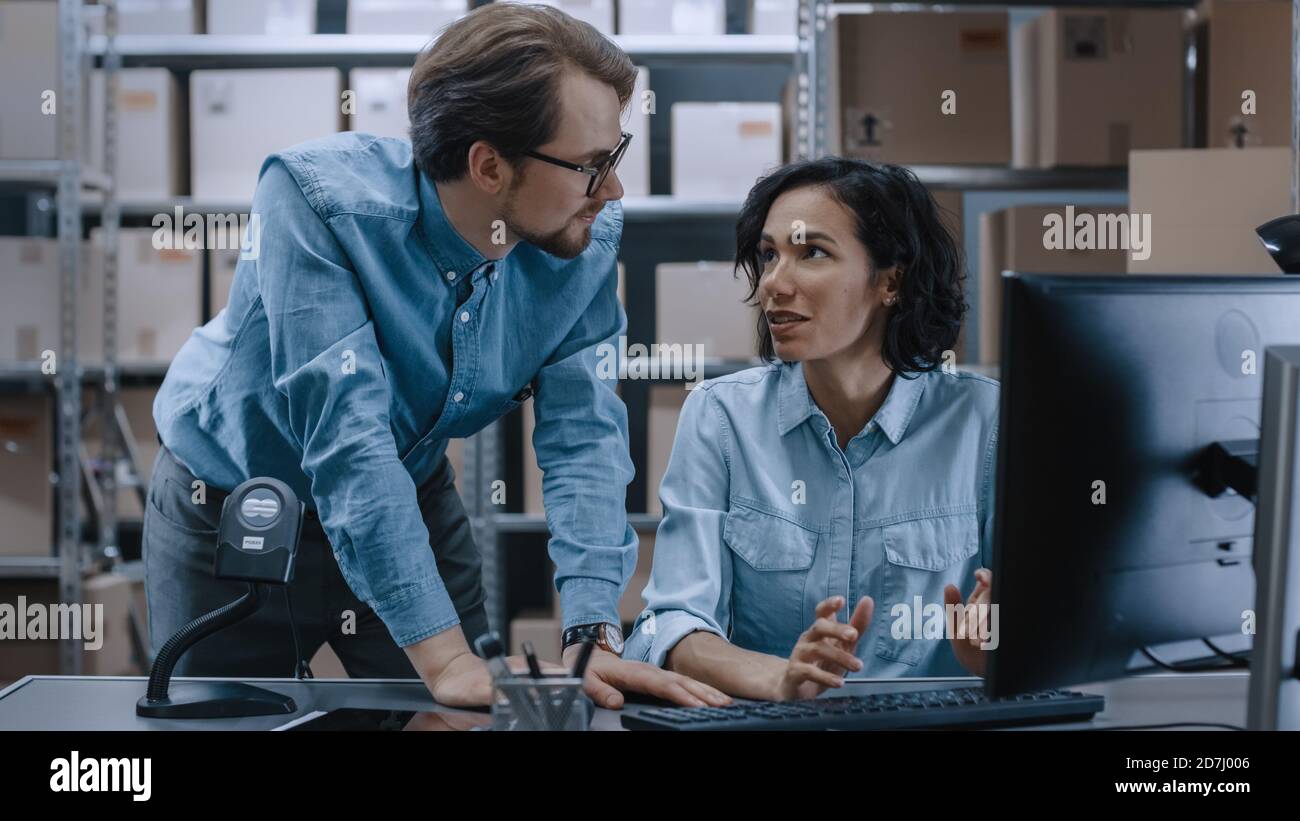 Les responsables des stocks d'entrepôt hommes et femmes parlent, résolvent les problèmes, utilisent un ordinateur personnel et vérifie le stock. Dans les rangées d'étagères en arrière-plan Banque D'Images