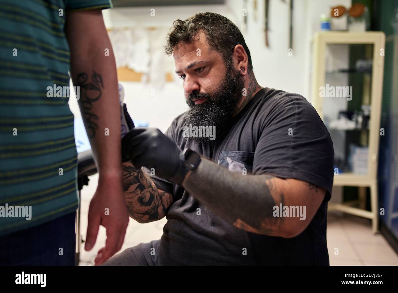 Un artiste mâle barbu tatouant la main de l'homme en studio Banque D'Images
