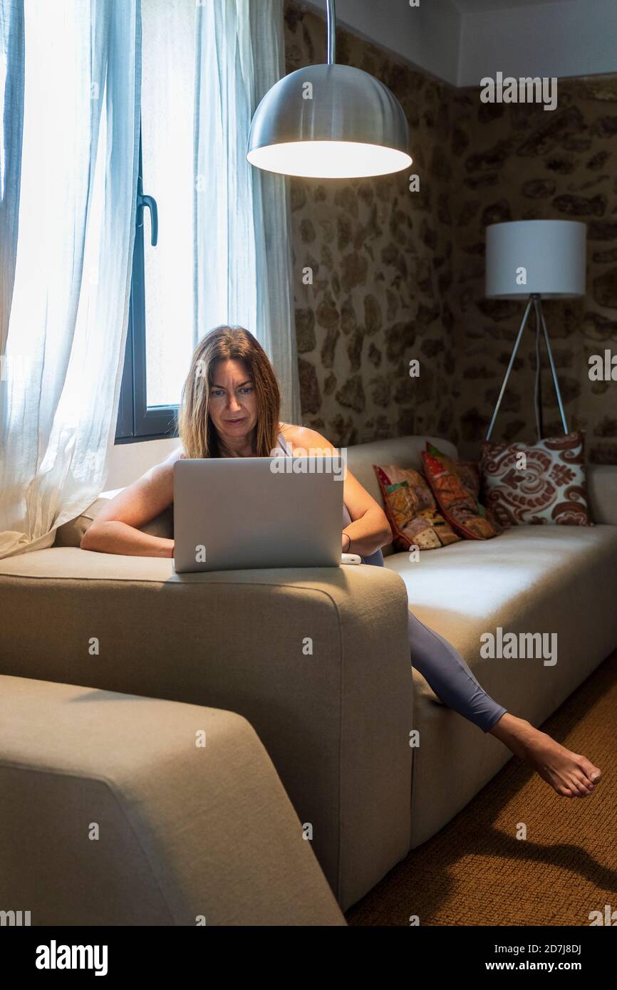 Femme travaillant sur un ordinateur portable tout en étant assise sur un canapé à la maison Banque D'Images