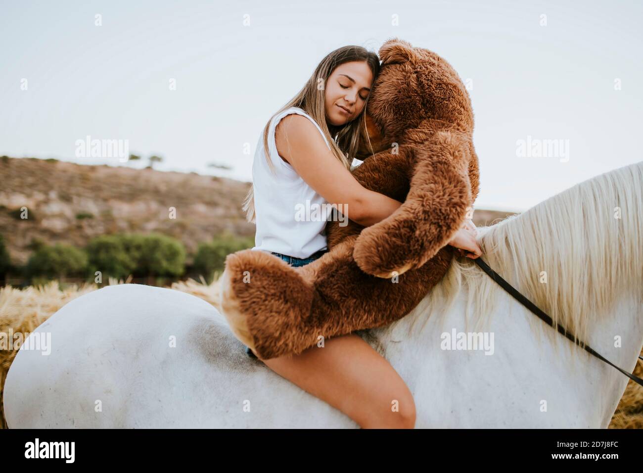 Portrait d'une jeune femme qui embrasse un grand ours en peluche pendant assis à cheval avec les yeux fermés Banque D'Images