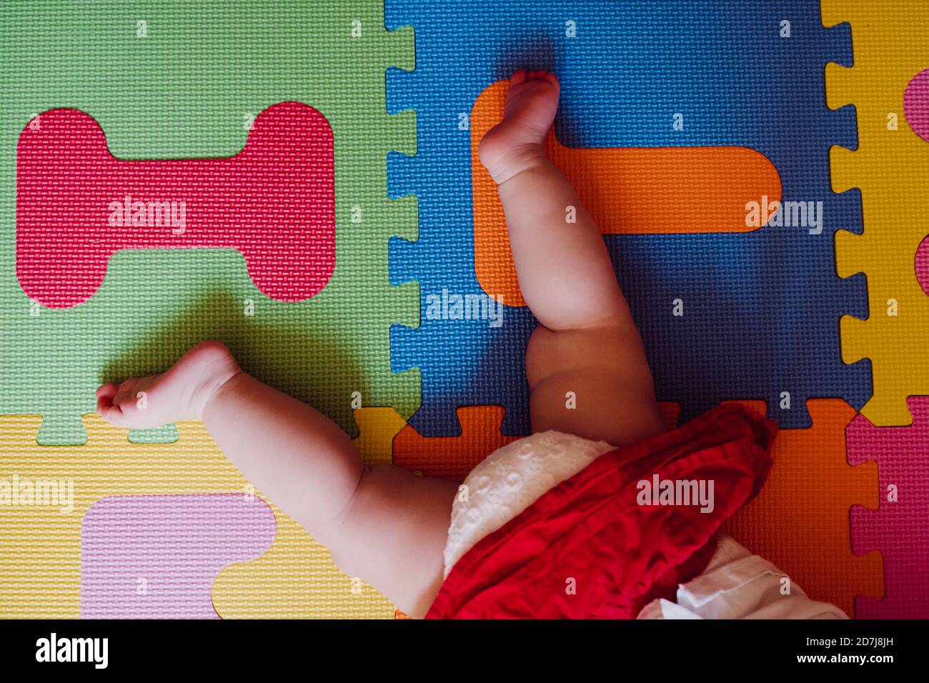 Jambes de bébé fille allongé sur un tapis de jeu de puzzle coloré à accueil Banque D'Images