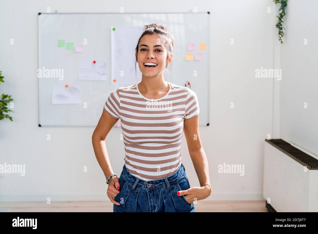 Belle femme architecte debout avec les mains dans les poches contre tableau blanc sur le lieu de travail Banque D'Images