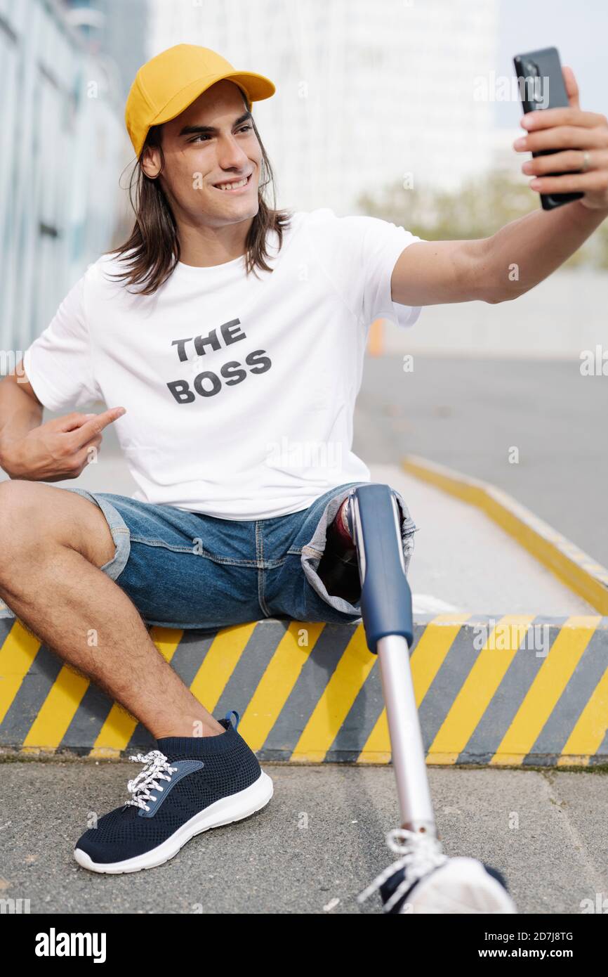 Homme avec un membre et un pied artificiels prenant le selfie tout en étant assis sur route en ville Banque D'Images