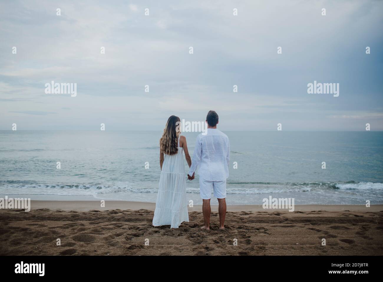 Couple tenant les mains tout en admirant la vue sur la mer se tenant sur la plage Banque D'Images