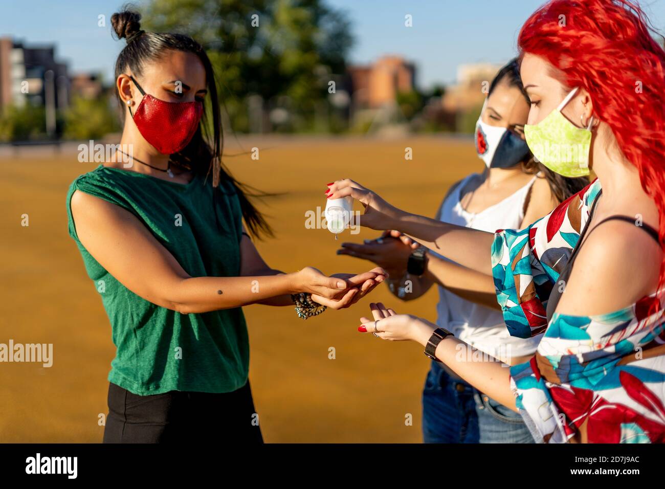 Amis utilisant un désinfectant pour les mains en se tenant à l'extérieur par temps ensoleillé Banque D'Images