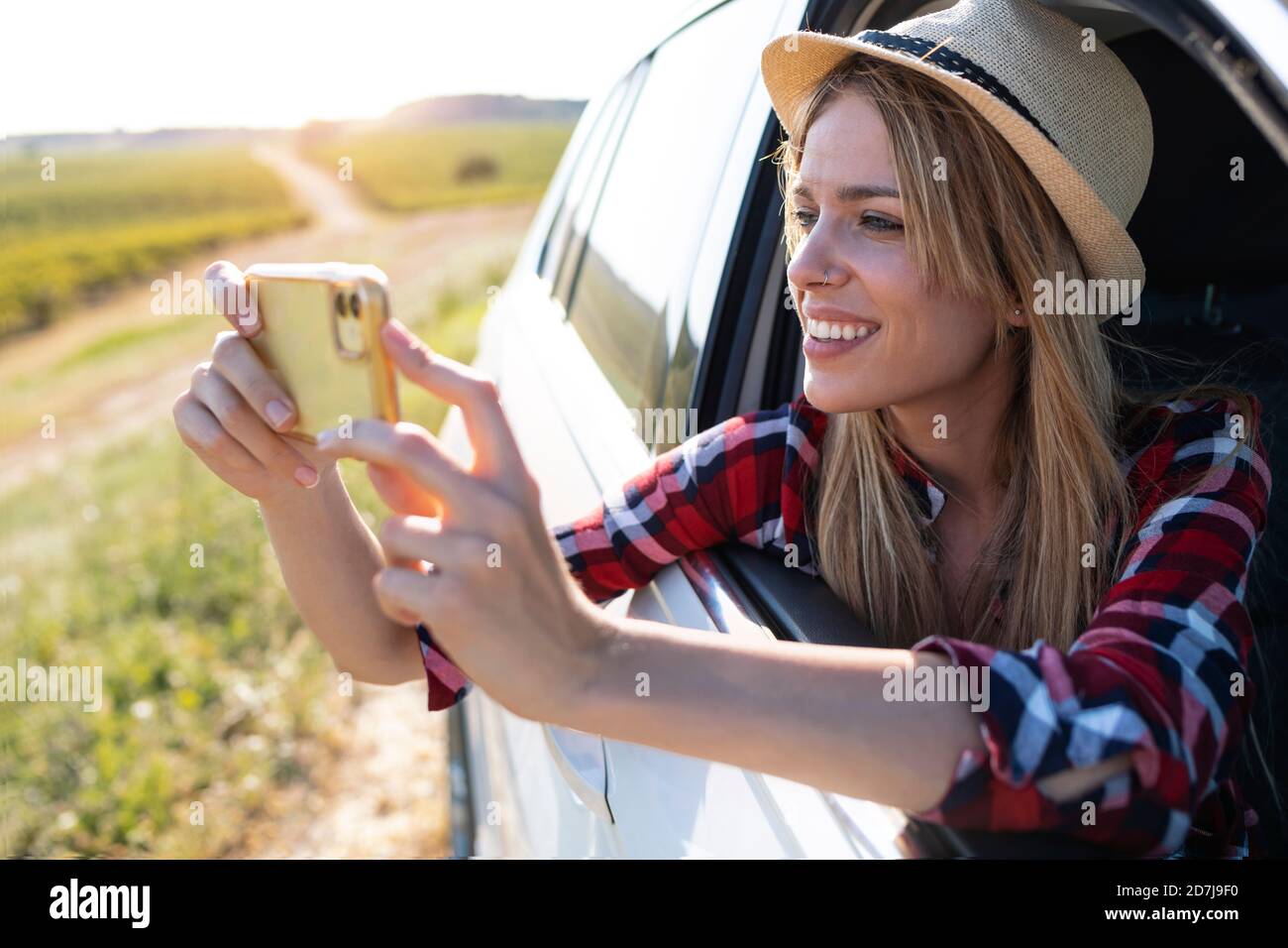 Jeune femme souriante prenant des photos par téléphone portable tout en étant assise en voiture Banque D'Images