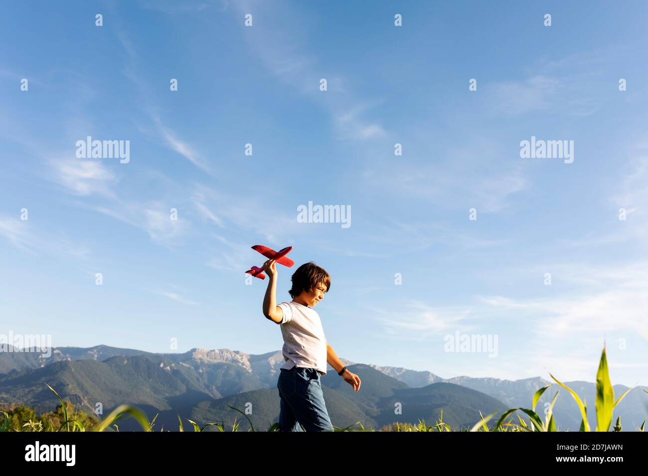 Garçon tenant un jouet d'avion tout en marchant contre le ciel clair Banque D'Images