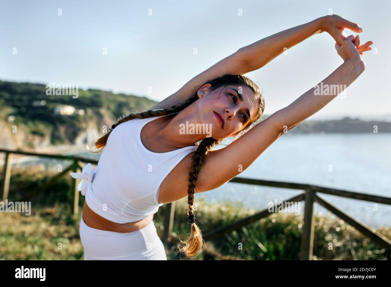 Jeune femme avec les bras relevés regardant loin tout en faisant de l'exercice contre ciel clair au coucher du soleil Banque D'Images
