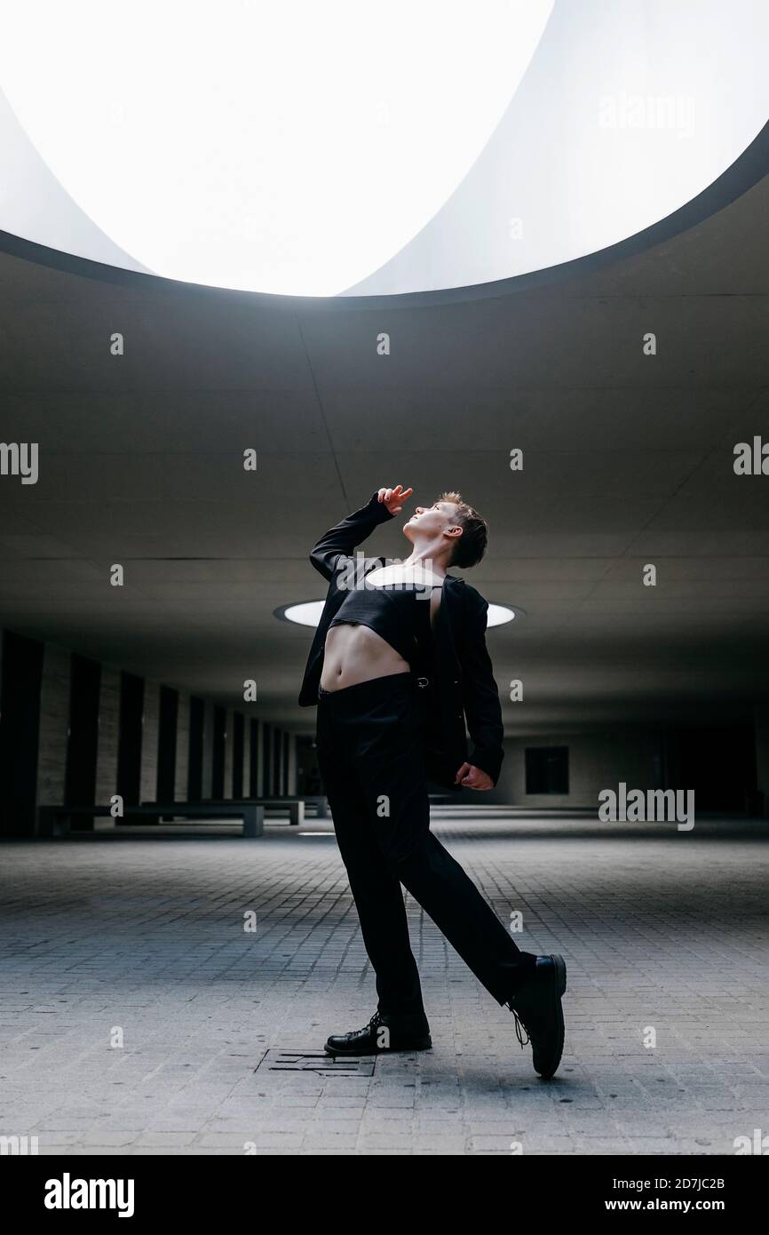 Jeune homme non binaire dansant sur le sol sous lumière éclairée sous-sol Banque D'Images