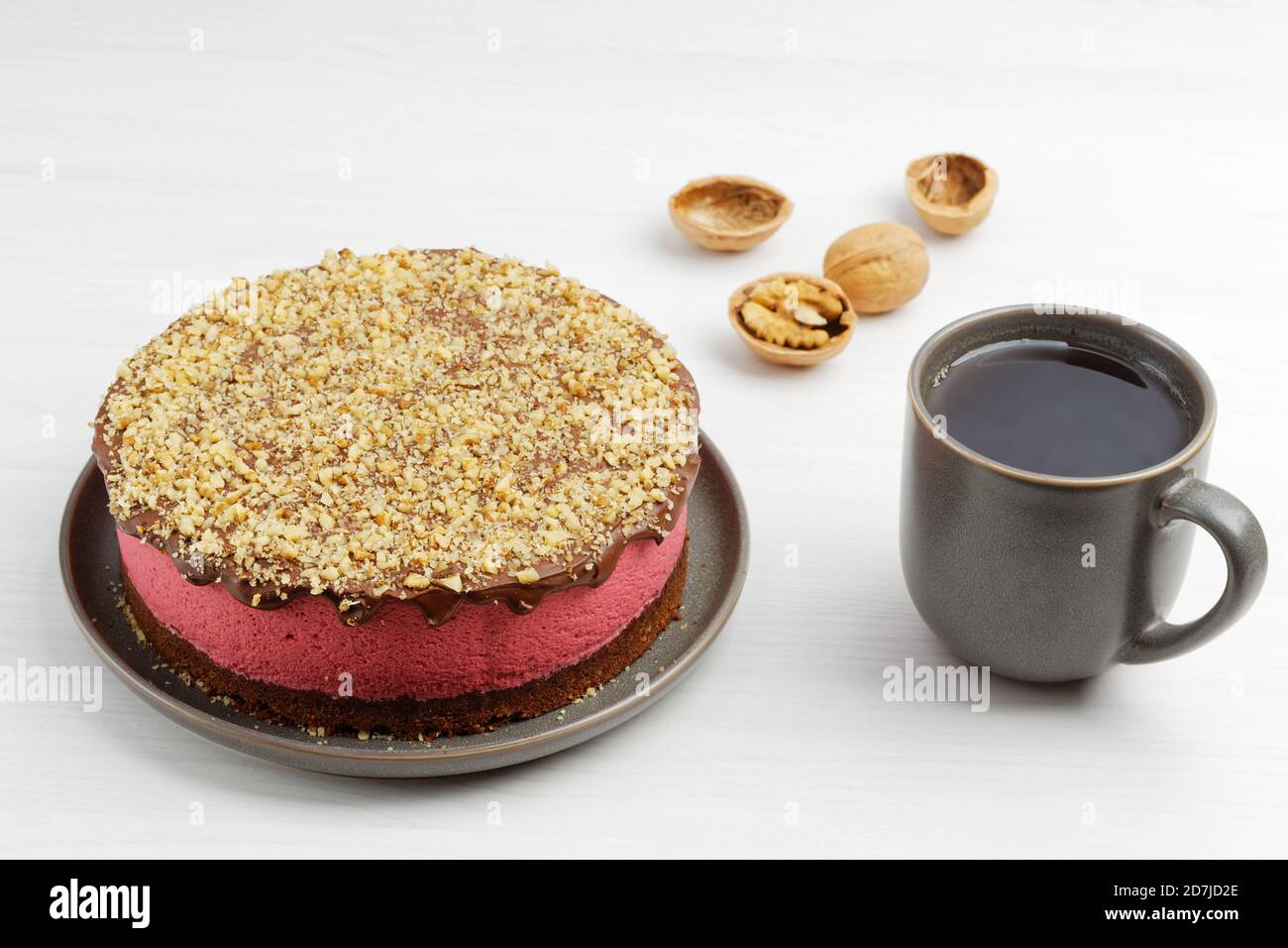 Cheesecake maison à la framboise arrosé de chapelure de noix et d'une tasse de thé sur table en bois blanc Banque D'Images