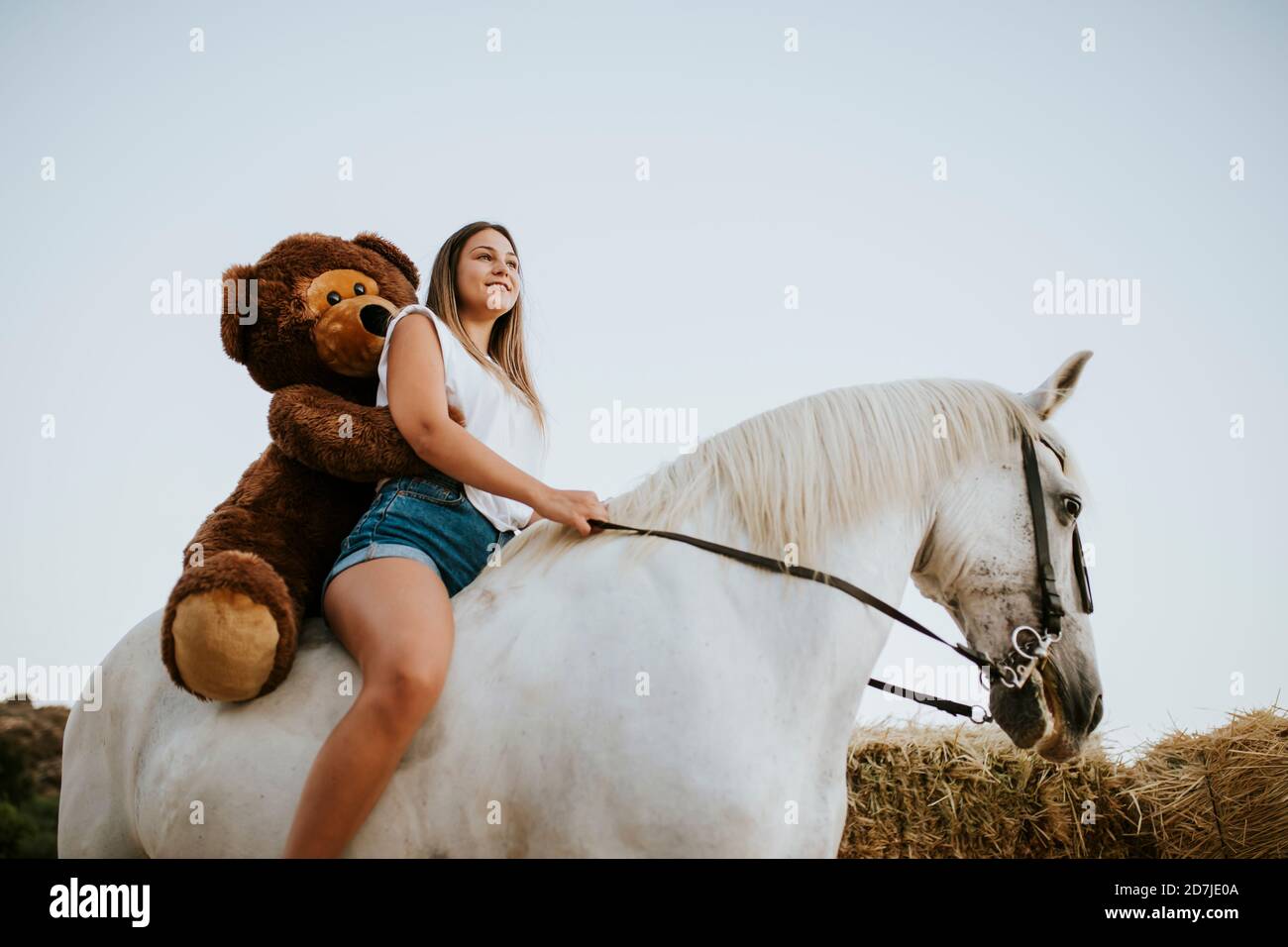 Belle jeune femme à cheval avec grand ours en peluche derrière Banque D'Images