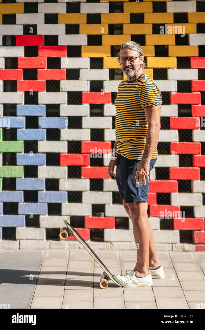 Homme mûr debout sur un skateboard contre un mur de briques de couleur Banque D'Images