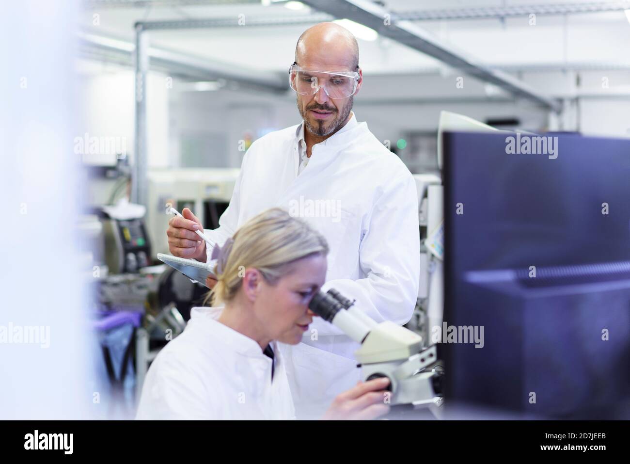 Un technicien de sexe masculin regarde une scientifique de sexe féminin qui fait de la recherche au microscope en laboratoire Banque D'Images