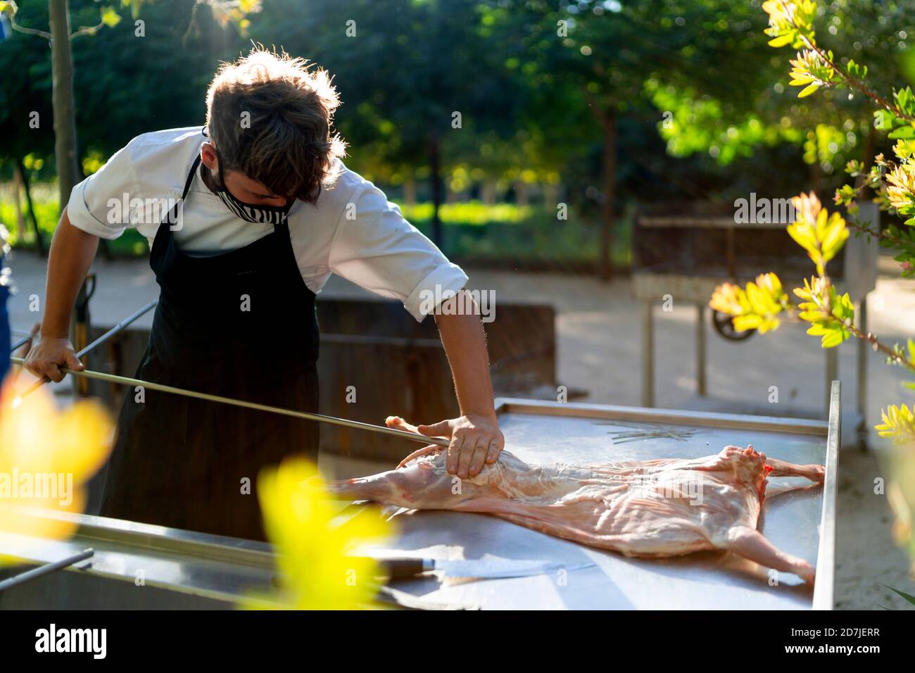 Chef masculin portant un masque coupant de la viande de chèvre sur la table pendant debout dans un verger Banque D'Images