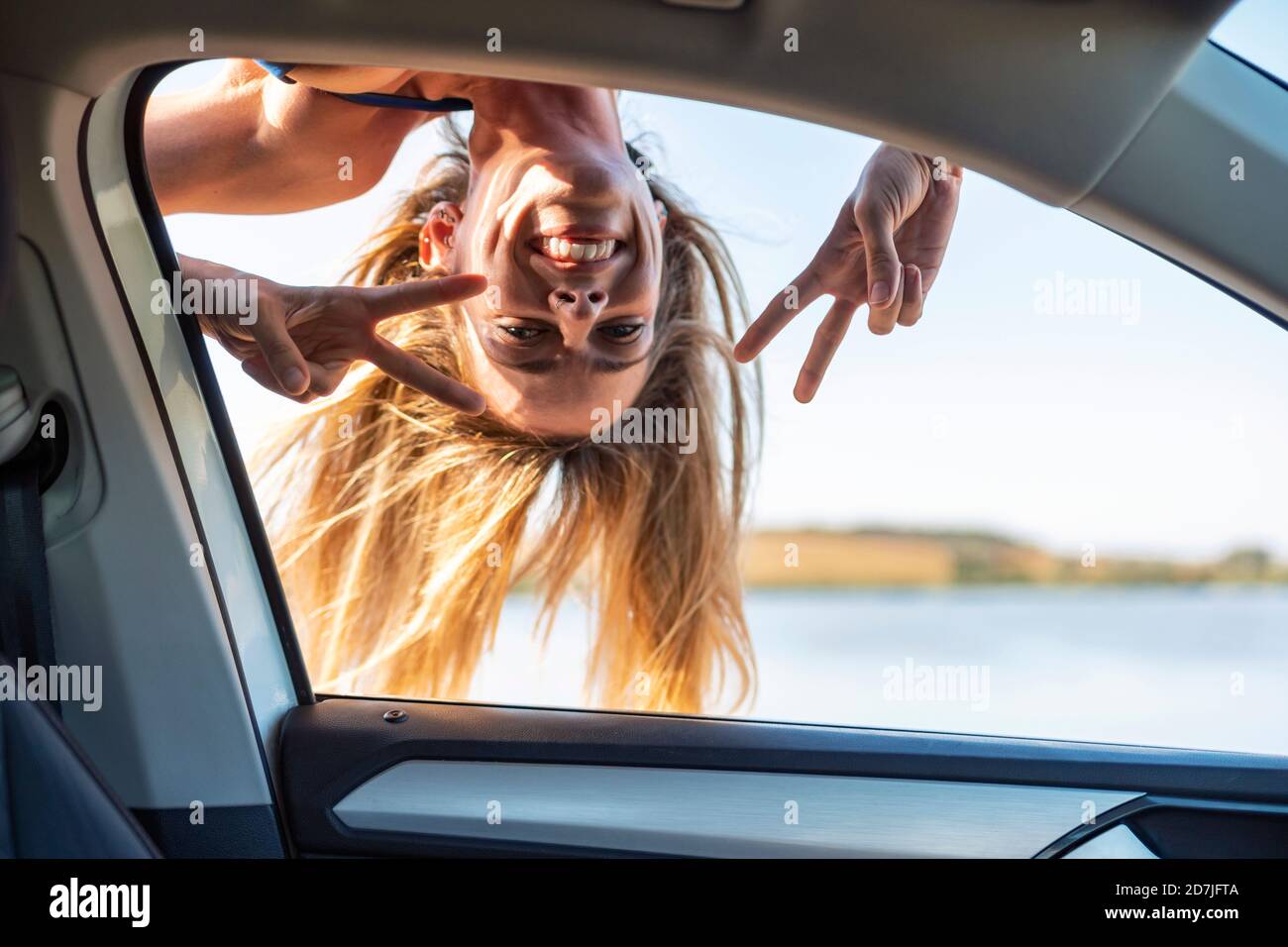 Femme insouciante montrant le signe de la paix en regardant par la fenêtre de voiture Banque D'Images