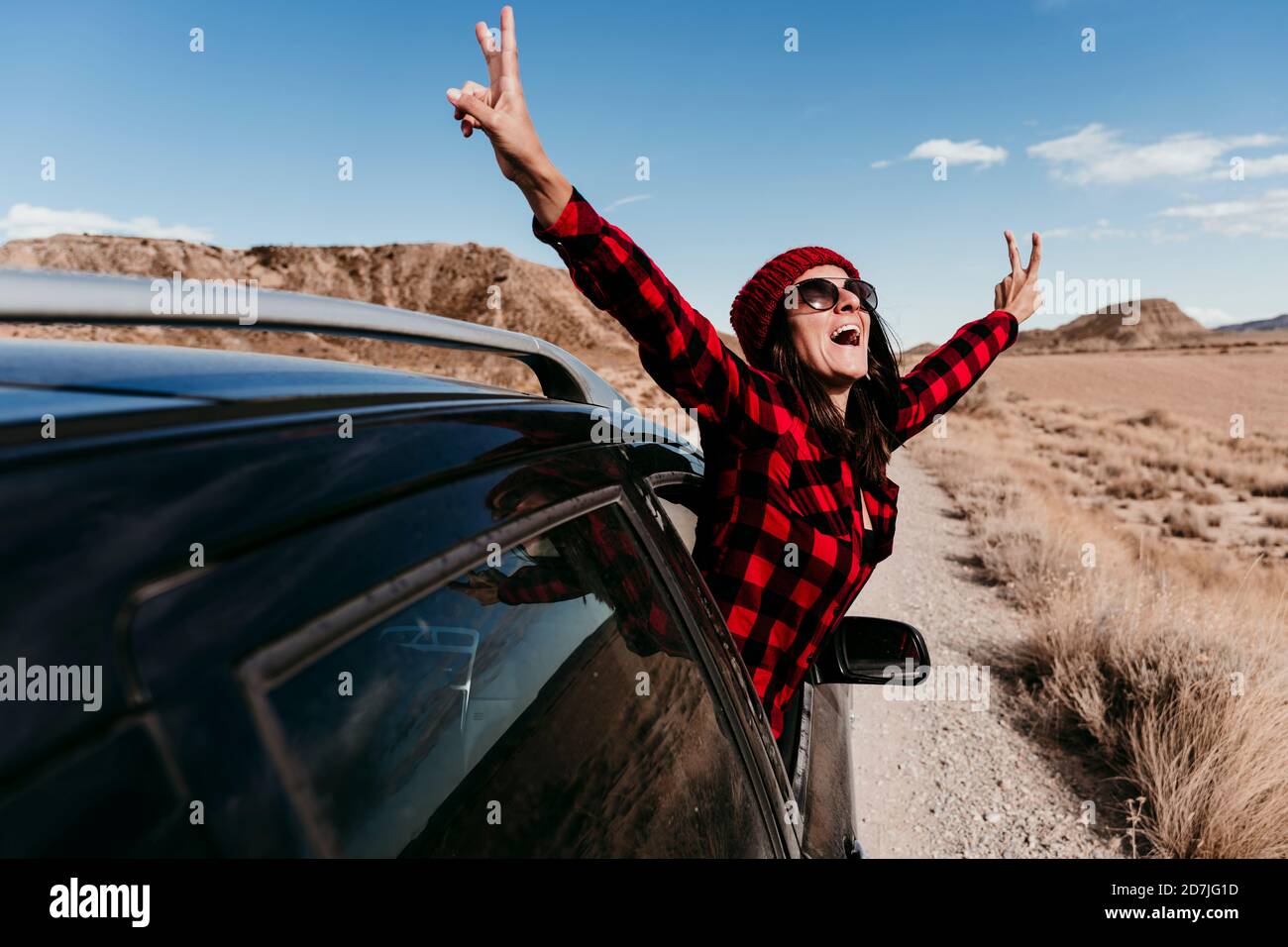 Espagne, Navarre, touriste féminine penchée hors de la fenêtre de voiture faisant des gestes signe de paix sur la route de terre à Bardenas Reales Banque D'Images