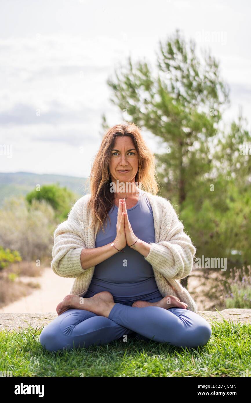 Femme faisant du yoga tout en étant assise sur l'herbe contre le ciel clair Banque D'Images