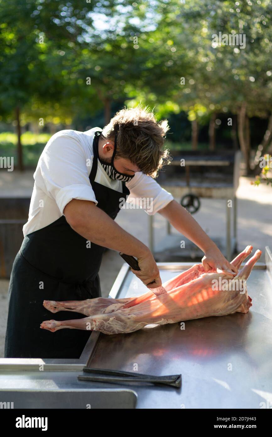 Chef masculin portant un masque coupant de la viande de chèvre sur la table pendant debout dans un verger Banque D'Images