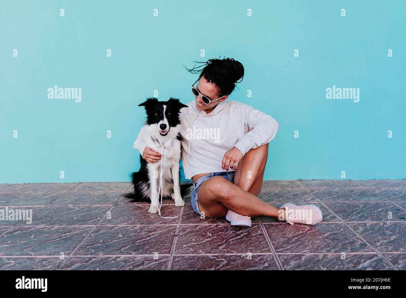 Bonne femme assise avec le bras autour de Border Collie chien contre mur turquoise Banque D'Images