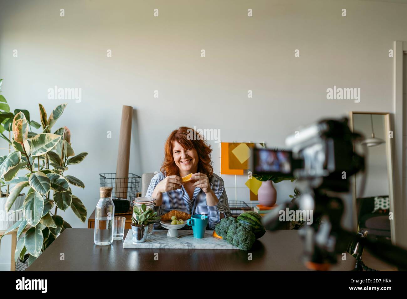 Femme souriante montrant des fruits frais tout en faisant vlog sur l'appareil photo à la maison Banque D'Images